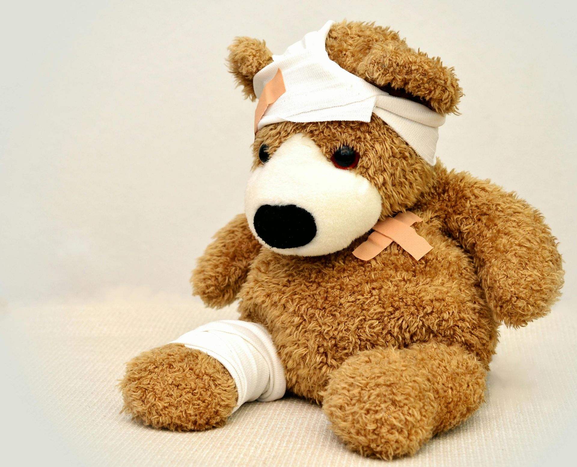 Brown teddy bear with bandaged head and leg, sitting on a light background