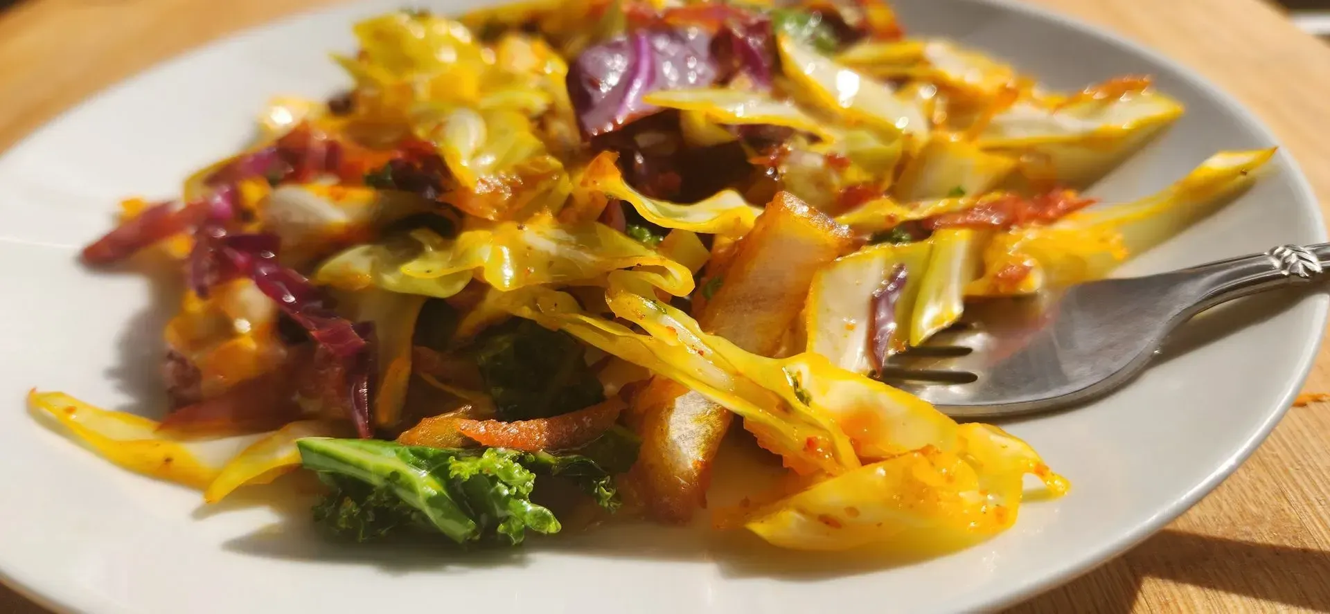 Plate of sauteed cabbage, broccoli, and red cabbage in a sauce, with a fork.