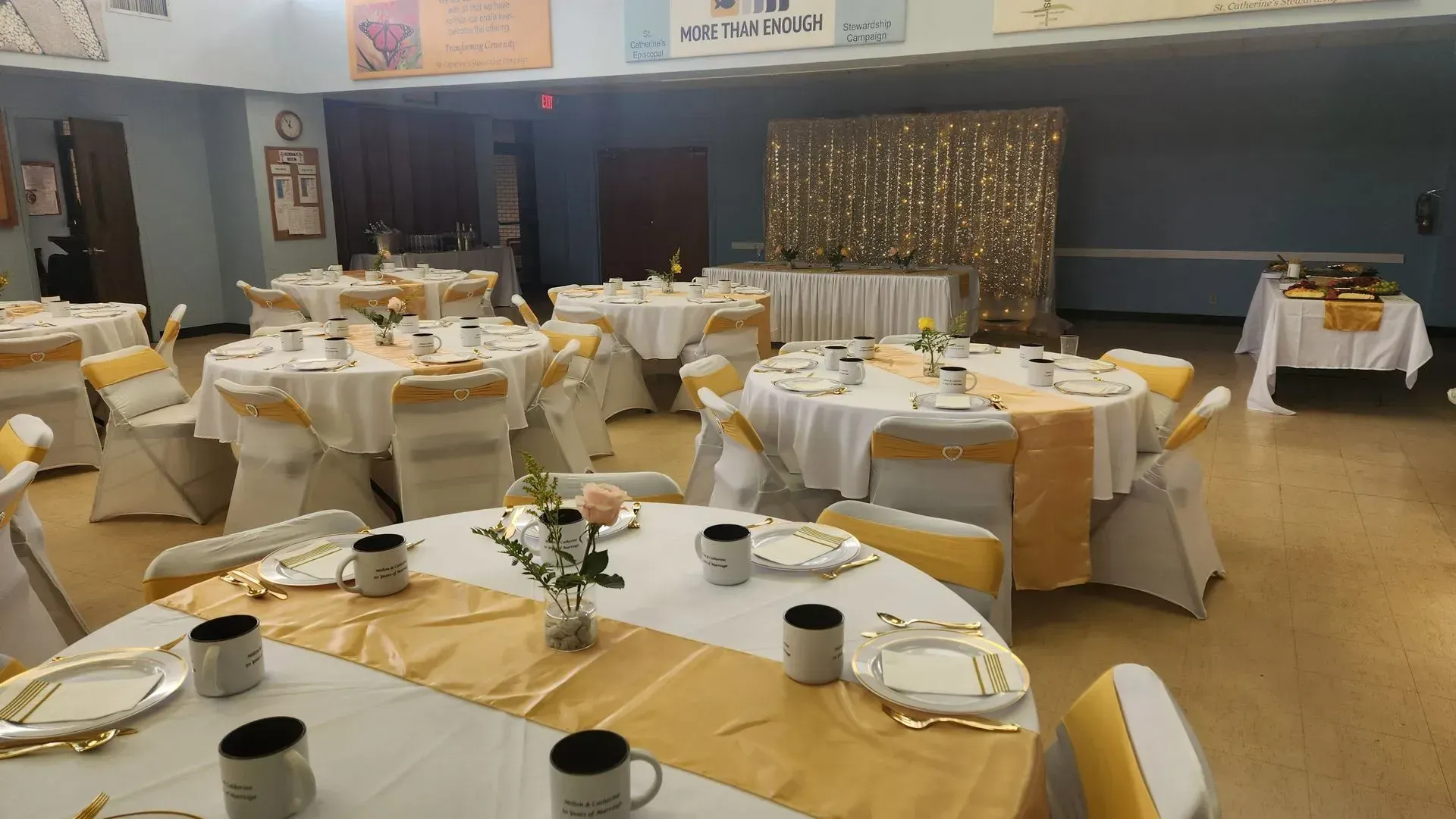 Banquet hall with round tables set for a celebration, gold and white decor.