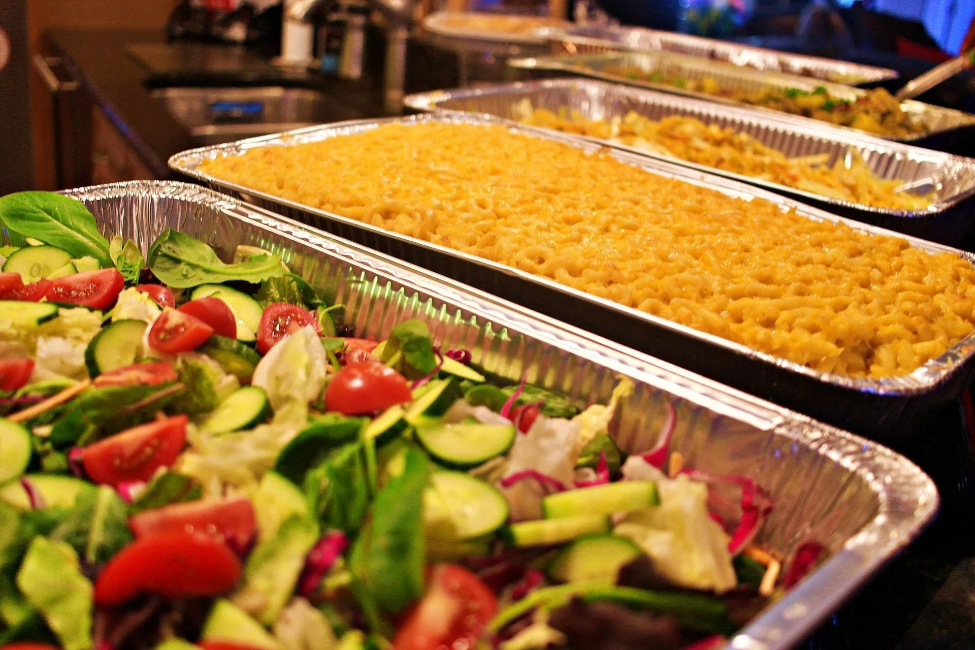 Salad, pasta, and other dishes in foil trays on a table, ready for serving.