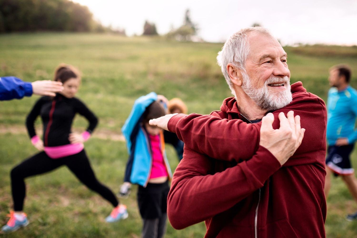 Older man stretching outdoors with a group during a fitness class