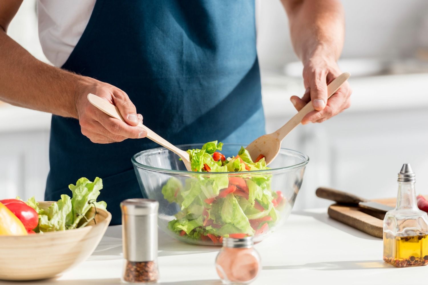 Person tossing salad in a glass bowl in a bright kitchen