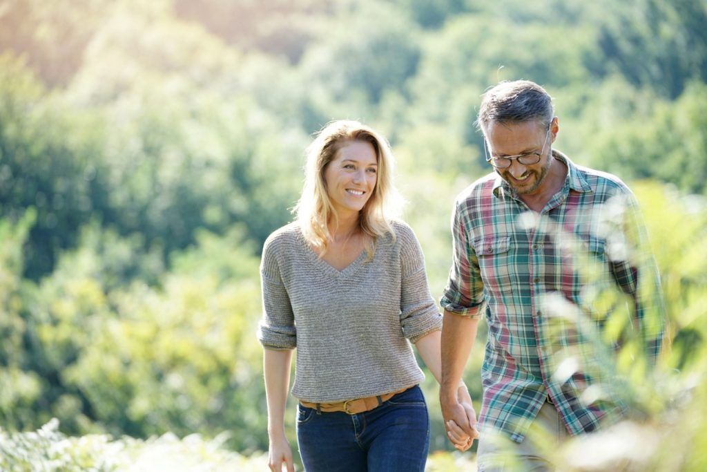 Two people walking hand in hand through a sunlit green field