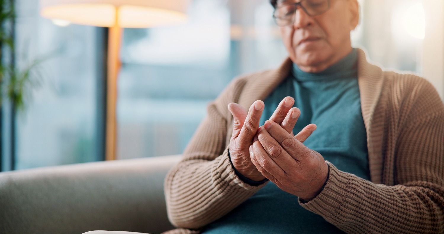Person seated on a couch, looking at and holding their hands in discomfort