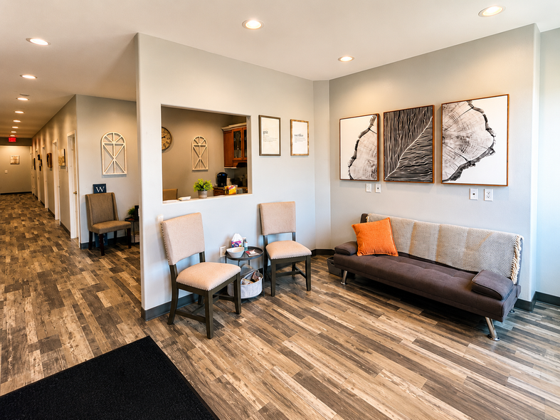 Bright modern apartment lobby with gray couch, framed art, hallway, and wood-look flooring.