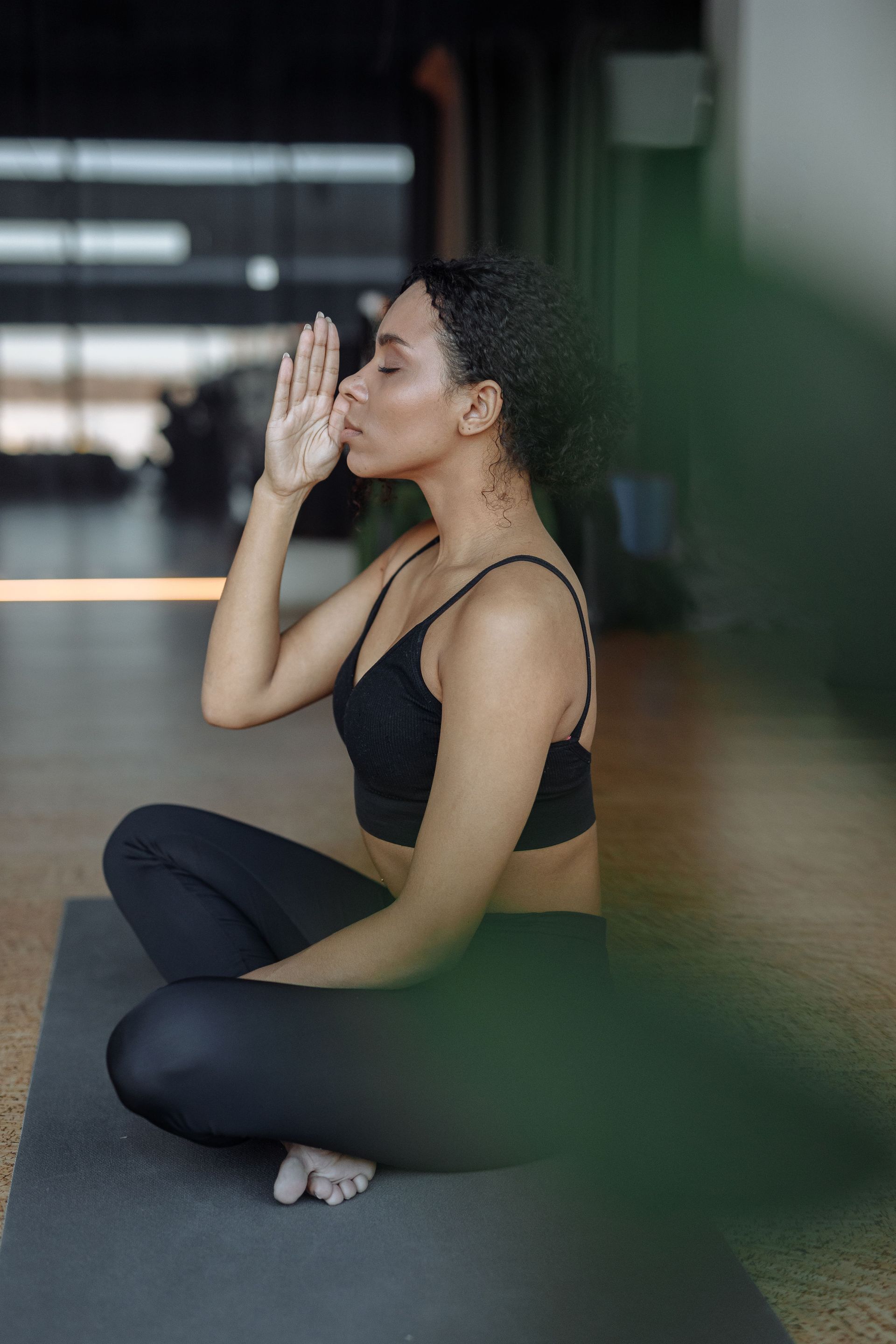 Woman in black activewear seated cross-legged, practicing breathing or meditation indoors