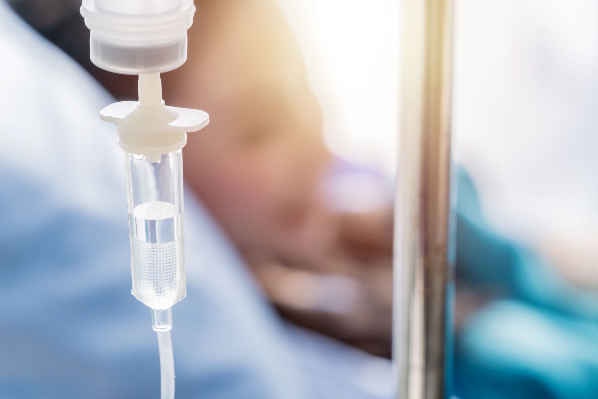 IV drip in a hospital setting with clear fluid in a plastic drip chamber.
