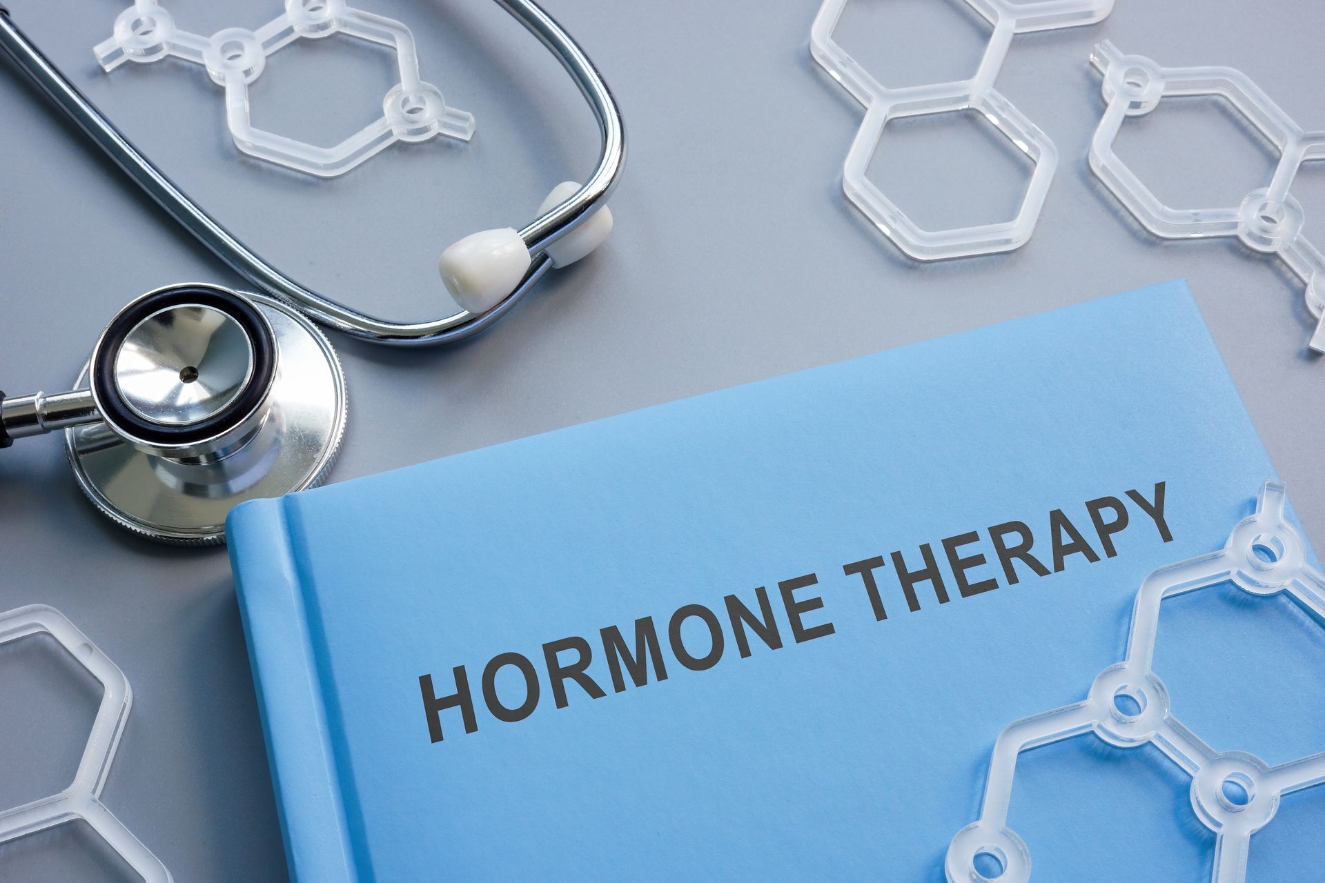 Blue folder labeled “Hormone Therapy” with a stethoscope and molecular models on a medical desk
