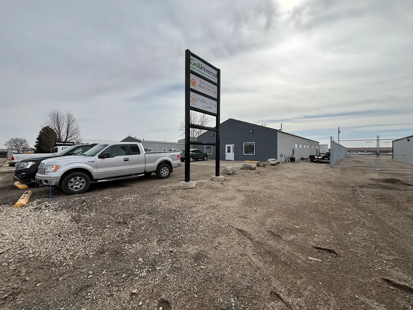 Gravel parking lot with a silver pickup, business sign, and gray buildings under a cloudy sky