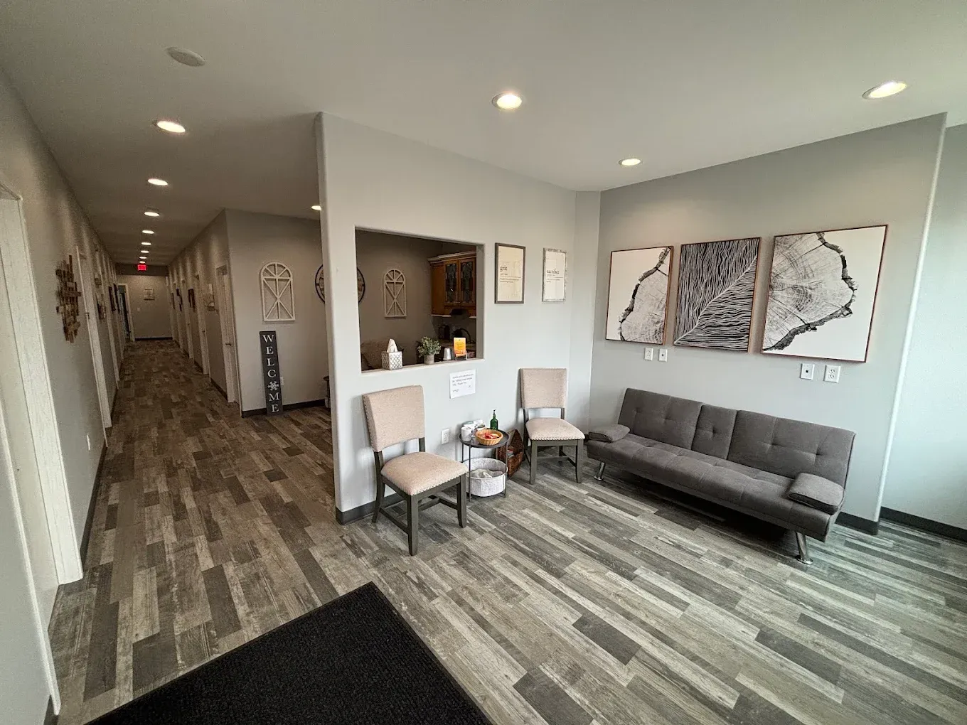 Bright modern apartment lobby with gray couch, framed art, hallway, and wood-look flooring.