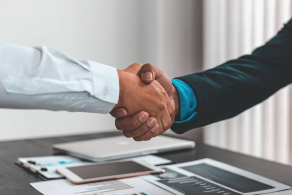 Two men are shaking hands over a table.