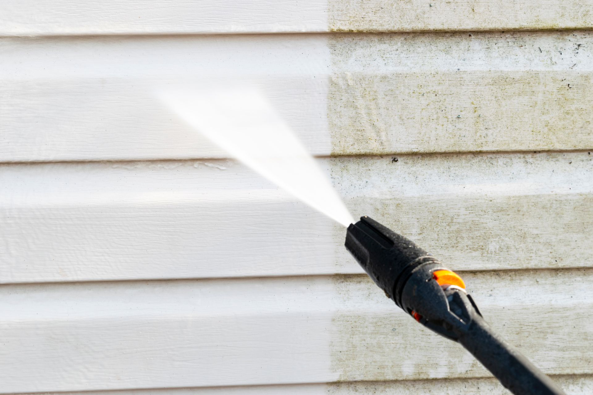 A pressure washer cleaning dirty siding, revealing a clean white surface.