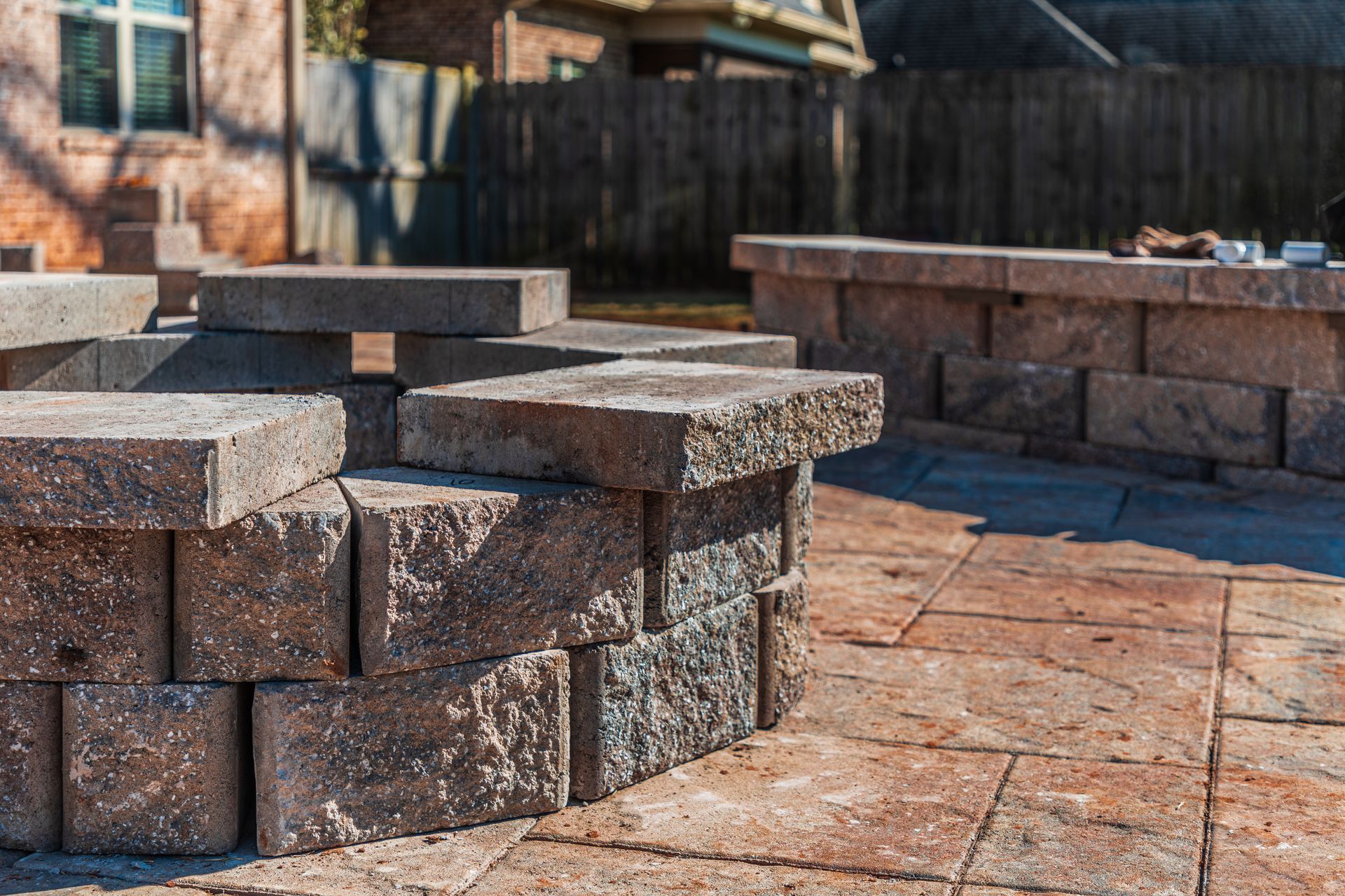 Stone fire pit and retaining wall constructed with gray and brown blocks on a paved patio.