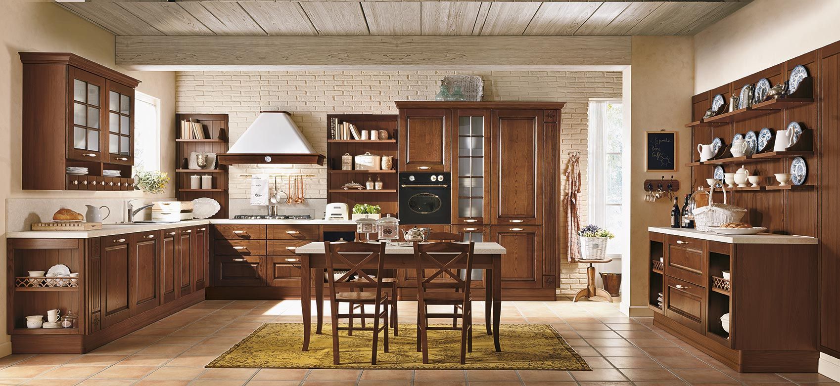 Interno accogliente della cucina con mobili in legno, tavolo da pranzo e scaffali su cui sono esposti piatti e oggetti decorativi.