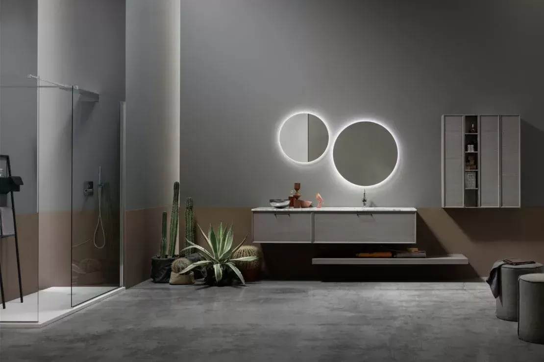 Bagno moderno grigio con doccia in vetro, mobile lavabo sospeso, specchi rotondi illuminati e pianta in vaso.