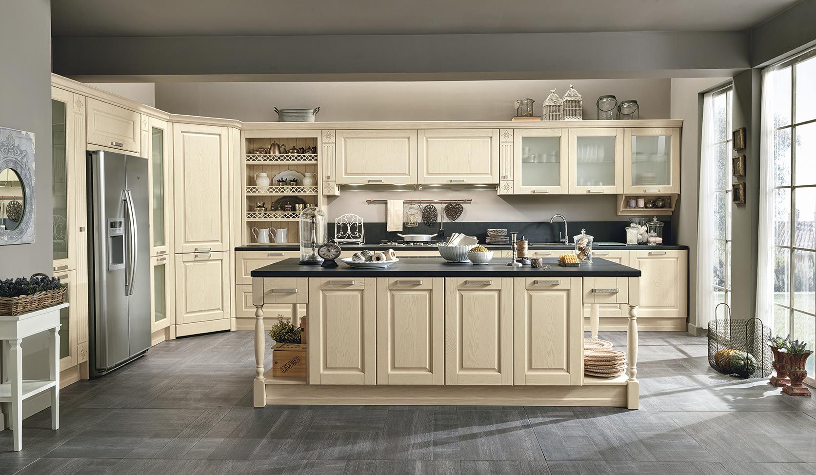 Cucina moderna e luminosa con mobili color crema, isola centrale, elettrodomestici in acciaio inossidabile e ampie finestre.