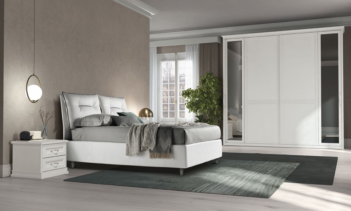 Camera da letto moderna bianca con letto, comodino, armadio e tappeto grigio su un pavimento chiaro.
