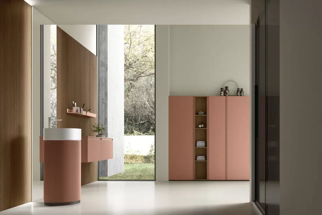 Interno moderno rosa e bianco con mobile da bagno, armadietto e vetrata a tutta altezza con vista sul verde.