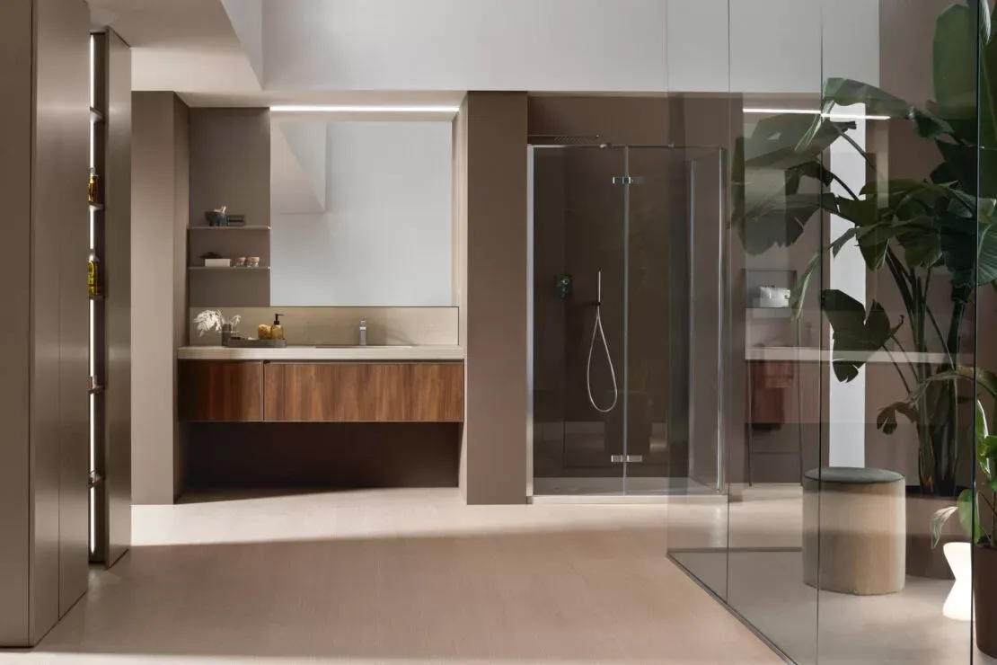Interno di un bagno moderno con mobile lavabo, specchio, box doccia in vetro e pianta in vaso.