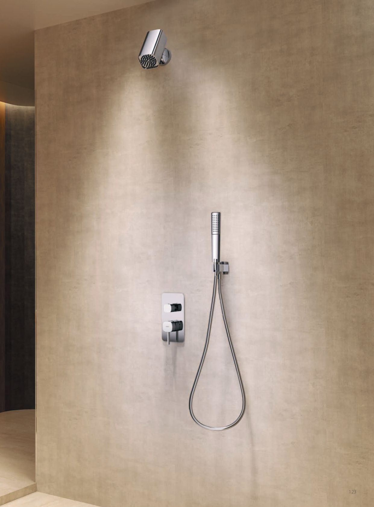 Parete doccia di hotel con doccetta a mano a parete e pannello di controllo su piastrelle beige.