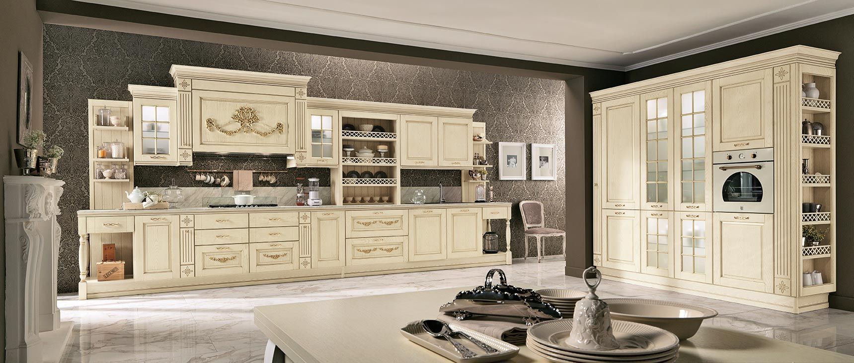 Cucina color crema con mobili, paraschizzi in pietra, isola e vetrina con forni a incasso.