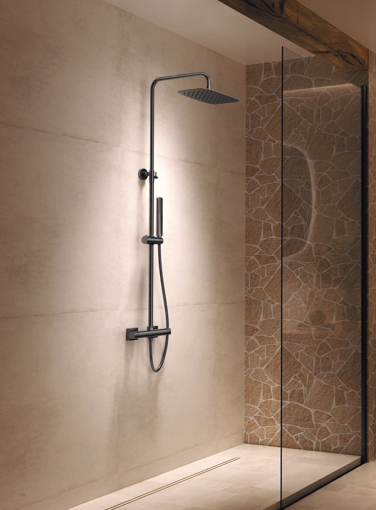Doccia moderna e minimalista con soffione a pioggia a parete e parete divisoria in vetro in un bagno piastrellato beige.