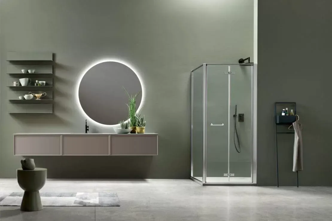 Bagno moderno grigio con mobile lavabo sospeso, specchio rotondo retroilluminato, box doccia in vetro e lavabo a parete.