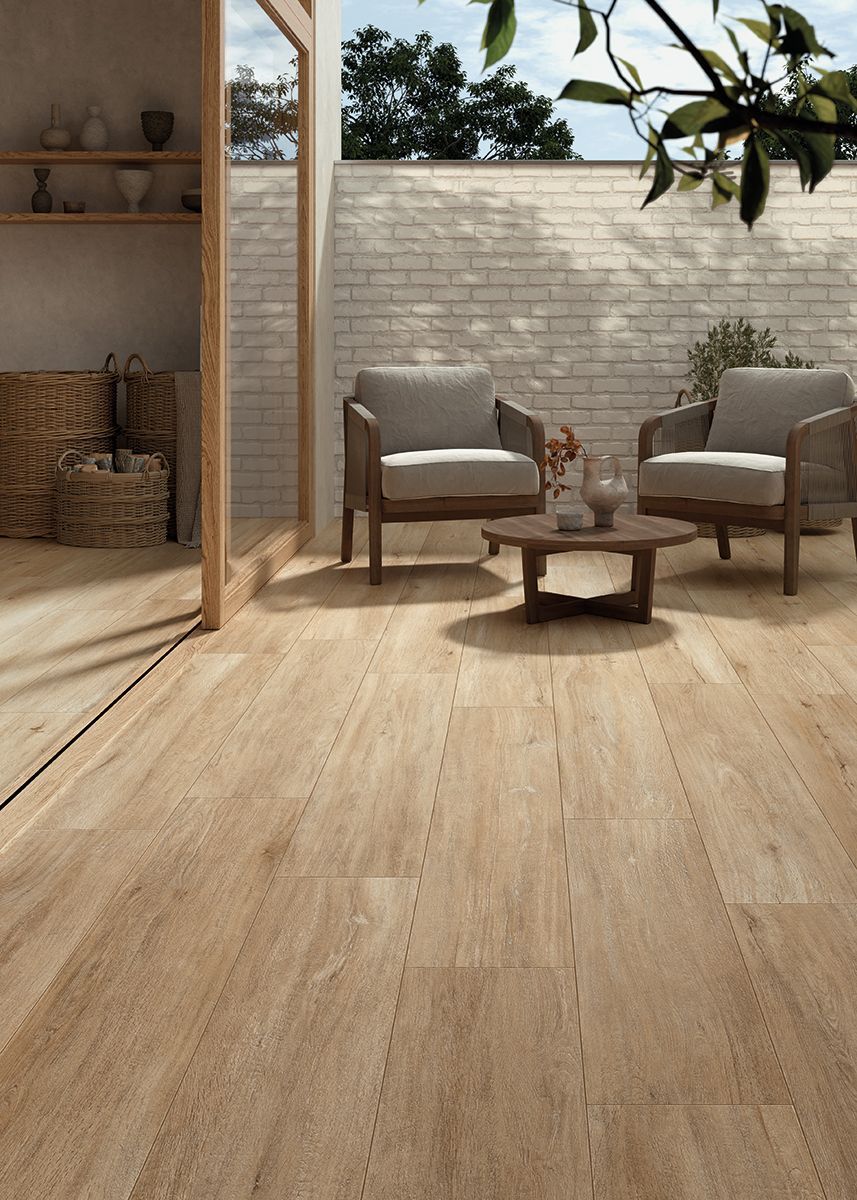 Patio soleggiato con due sedie, tavolo rotondo e decorazioni intrecciate su un pavimento in legno.