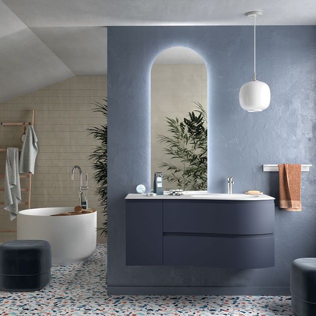 Bagno moderno con mobile lavabo blu, specchio ad arco, vasca freestanding e piastrelle a pavimento con effetto maculato.