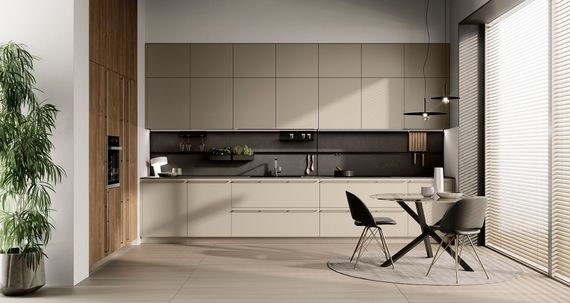 Cucina moderna e minimalista con mobili beige, paraschizzi nero e piccolo tavolo da pranzo accanto a una finestra luminosa.
