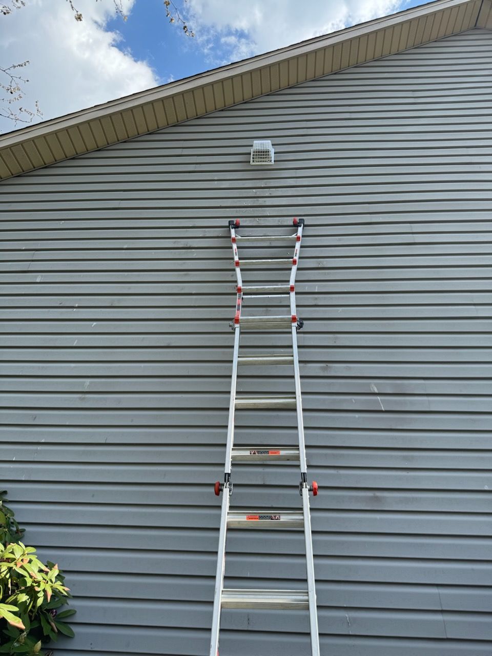 Extension ladder leaning against gray house siding under a blue sky