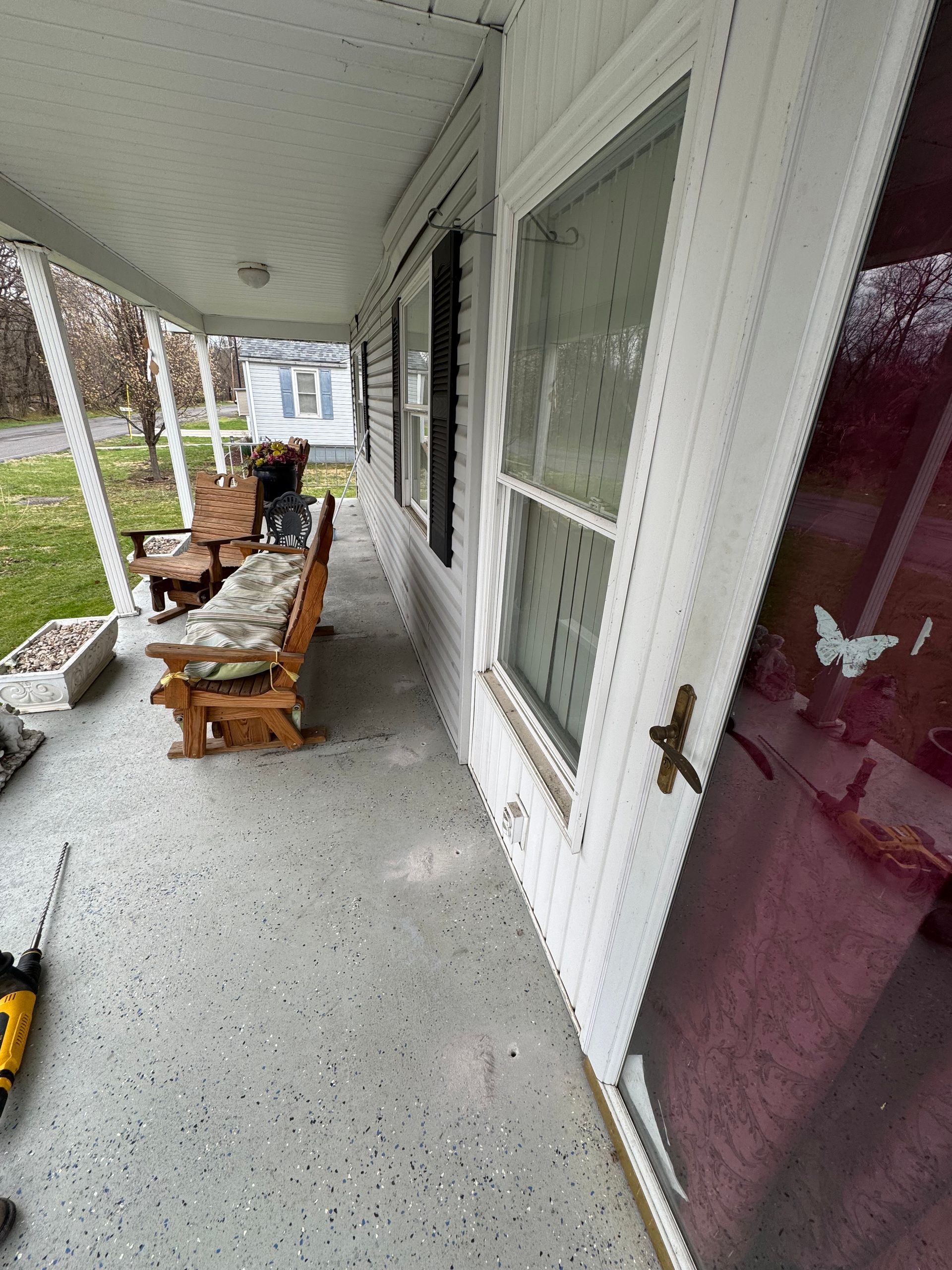 Covered porch with white siding, door, and bench.  A drill lays on the speckled floor.