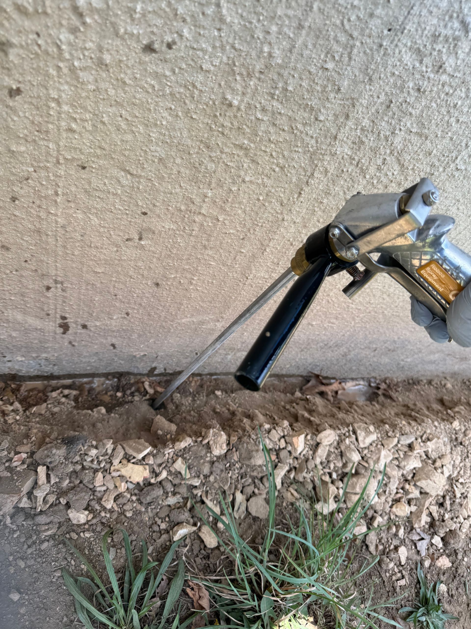 Person using a foam sealant gun to fill a gap between a concrete wall and the ground.