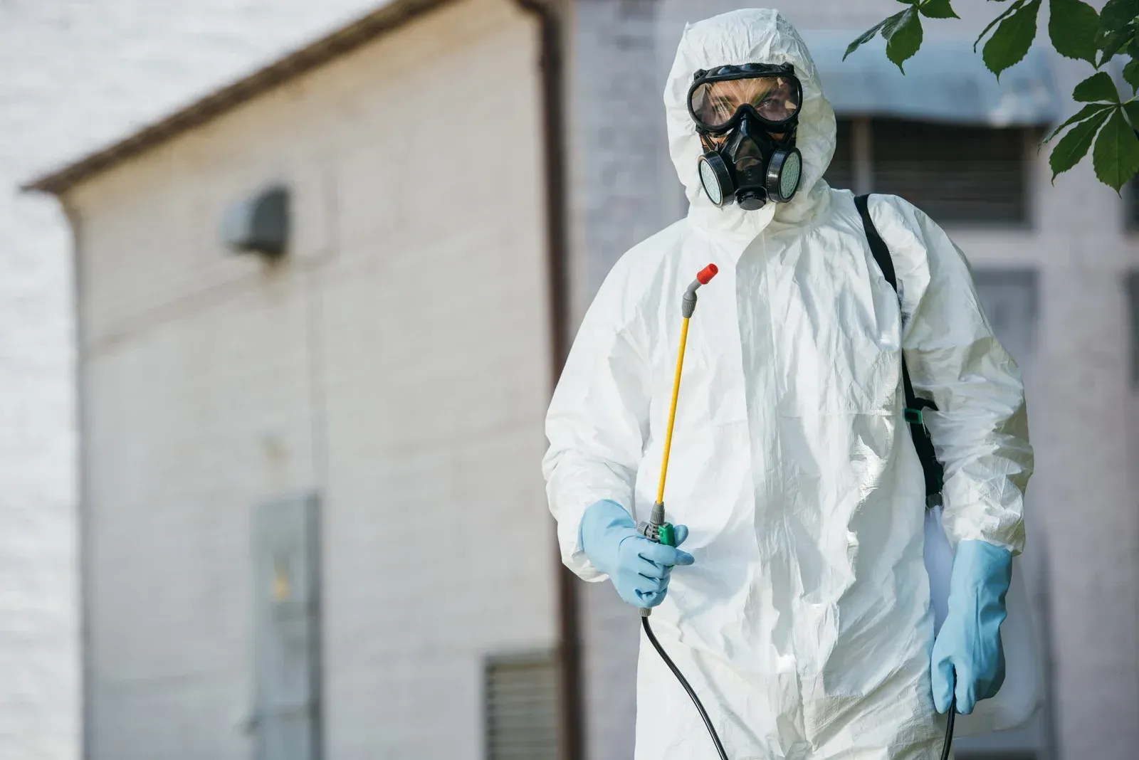 A man in a protective suit is spraying chemicals on a building.