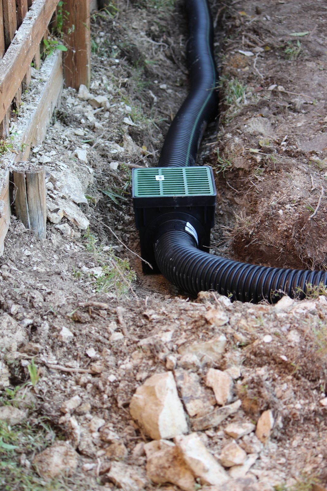A drain pipe is being installed in the dirt next to a wooden fence.