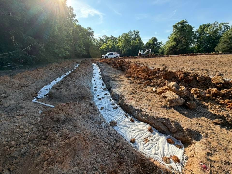 Eroded dirt trench lined with white fabric beside a muddy construction site and parked vehicle under trees