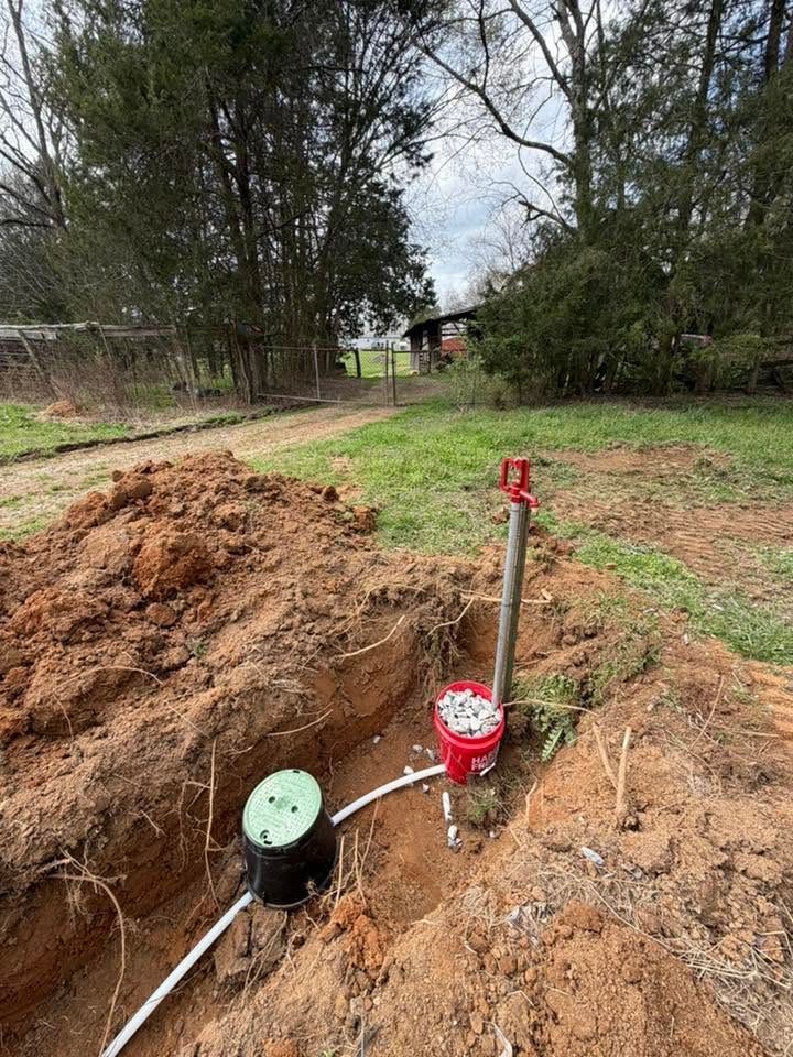 Trenched yard with two utility meters and pipes beside a grassy, wooded area