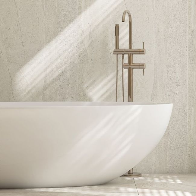 Minimalist white bathtub beside a brass faucet in a sunlit bathroom