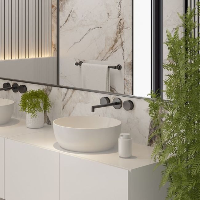 Minimalist bathroom vanity with white sink, black faucet, marble wall, and green plants