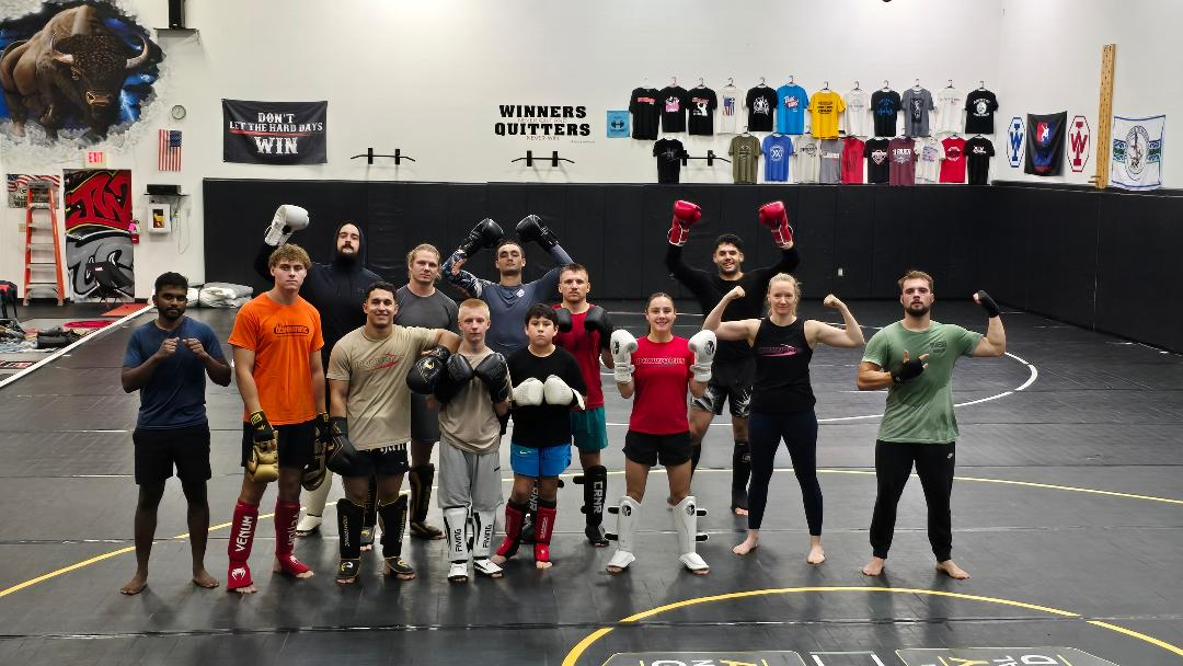 Group of people posing in a gym with weights and equipment in the background.