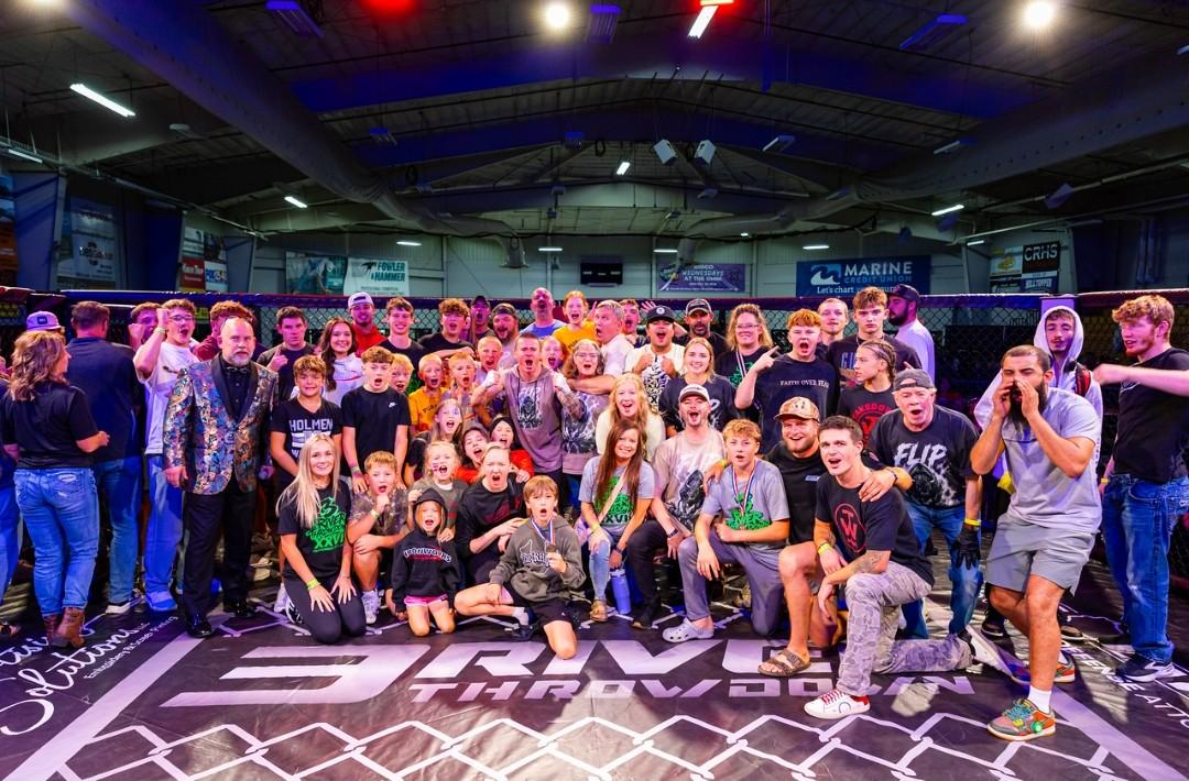 Large group posing on a stage at an indoor event, with colorful lights and patterned flooring.