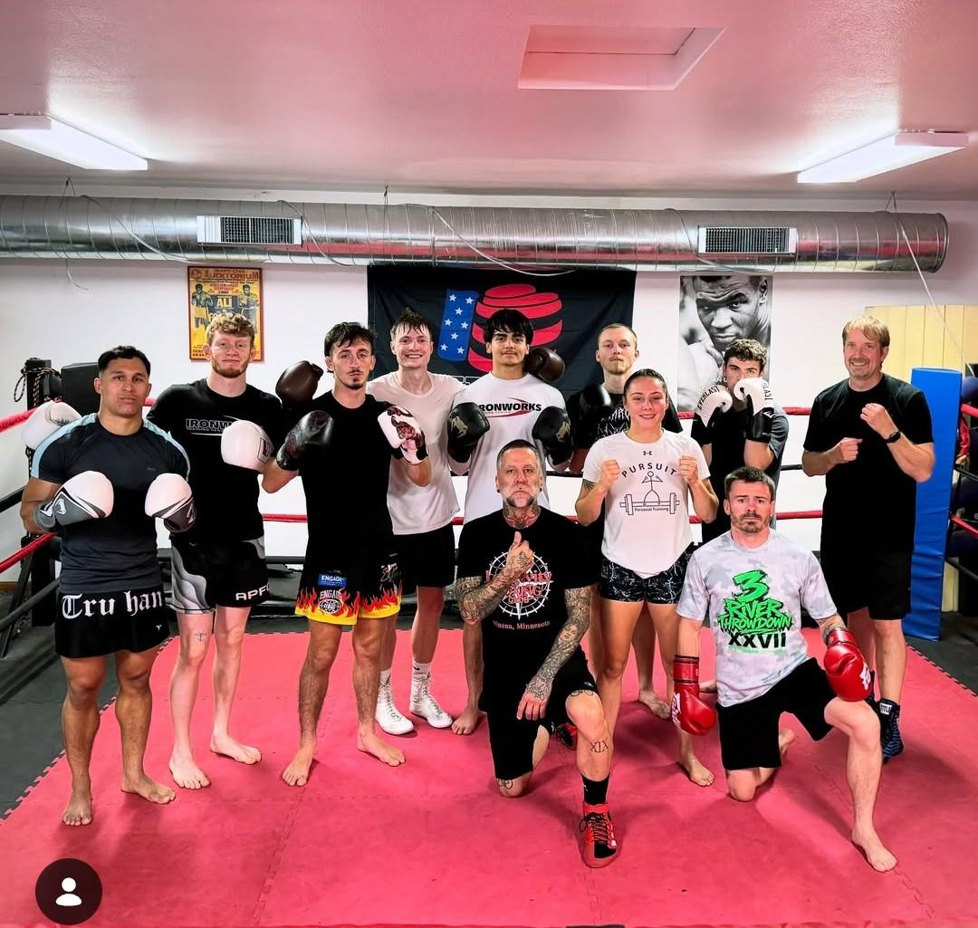 Group of people in a gym posing on pink mats, holding boxing gloves and smiling after training