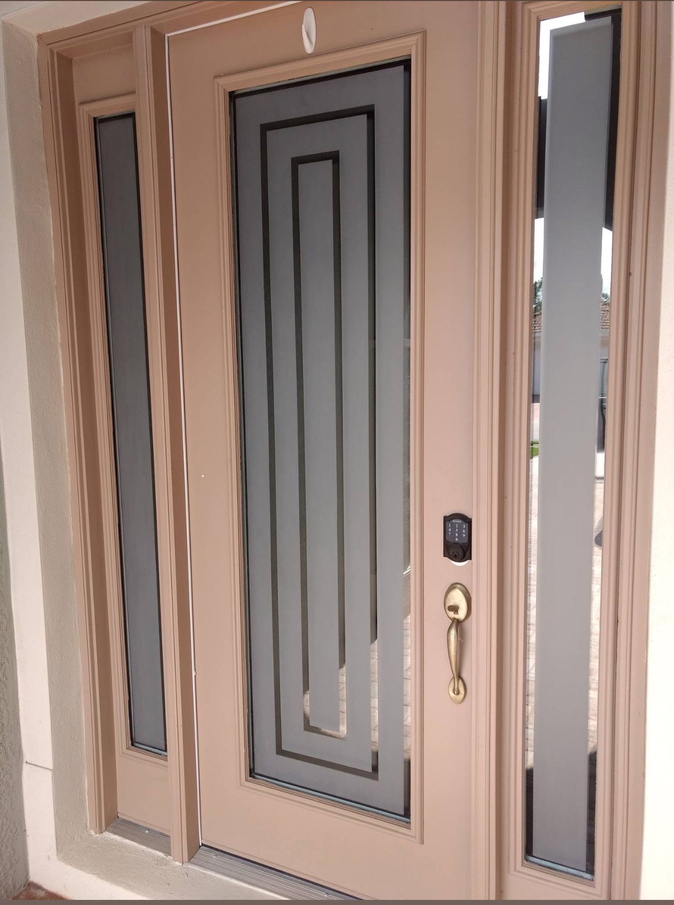 Beige front door with decorative glass panels and sidelights. Gold hardware.
