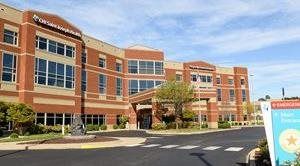 Exterior view of a three-story brick building with windows, likely a hospital. Sunny day with a blue sky.