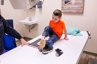 Boy in orange shirt has foot x-rayed at medical office.