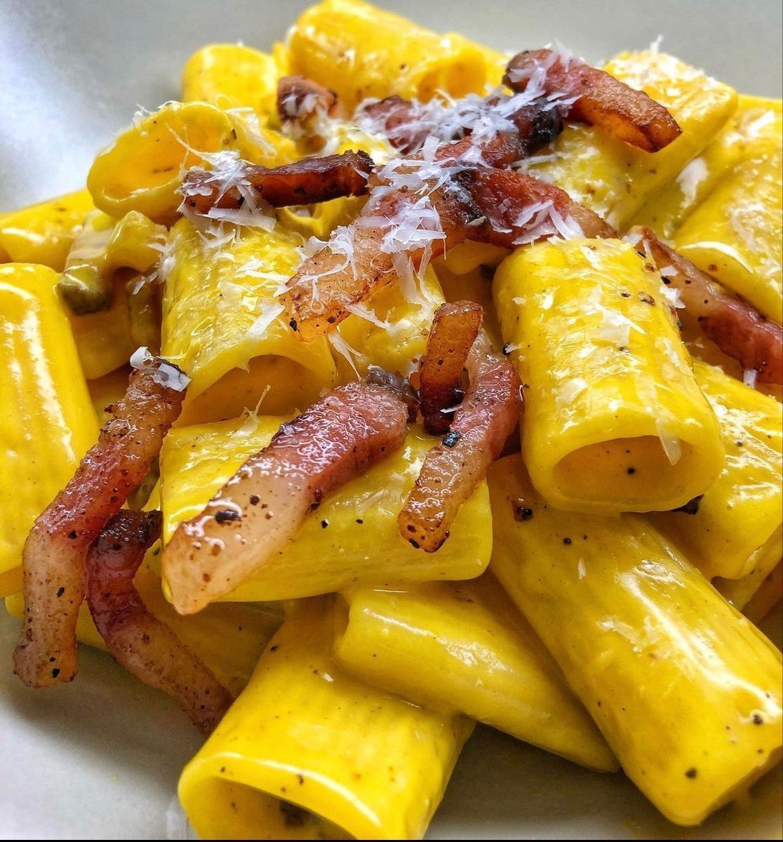 Rigatoni con una vivace salsa alla vodka arancione e pezzetti di pancetta, serviti in una ciotola bianca bassa.