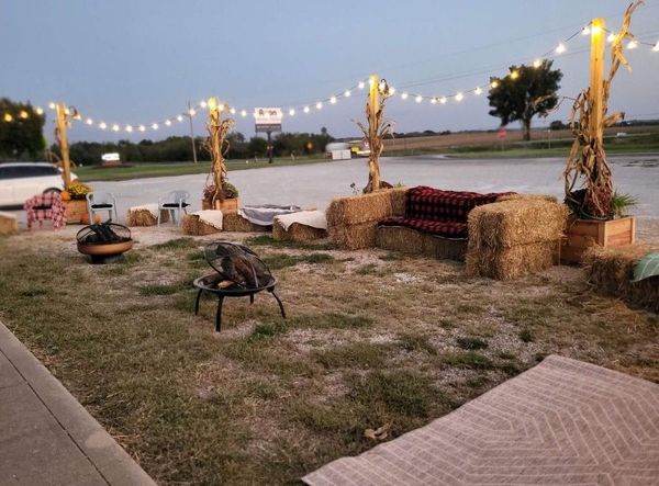Outdoor seating area with hay bale furniture, fire pits, string lights, and cornstalk decor.
