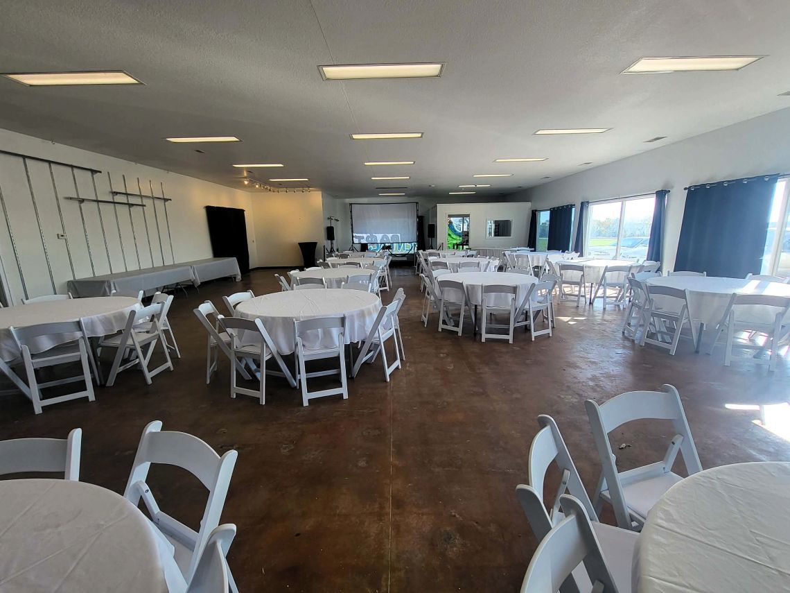 A large event space with round tables covered in white linens and white chairs.