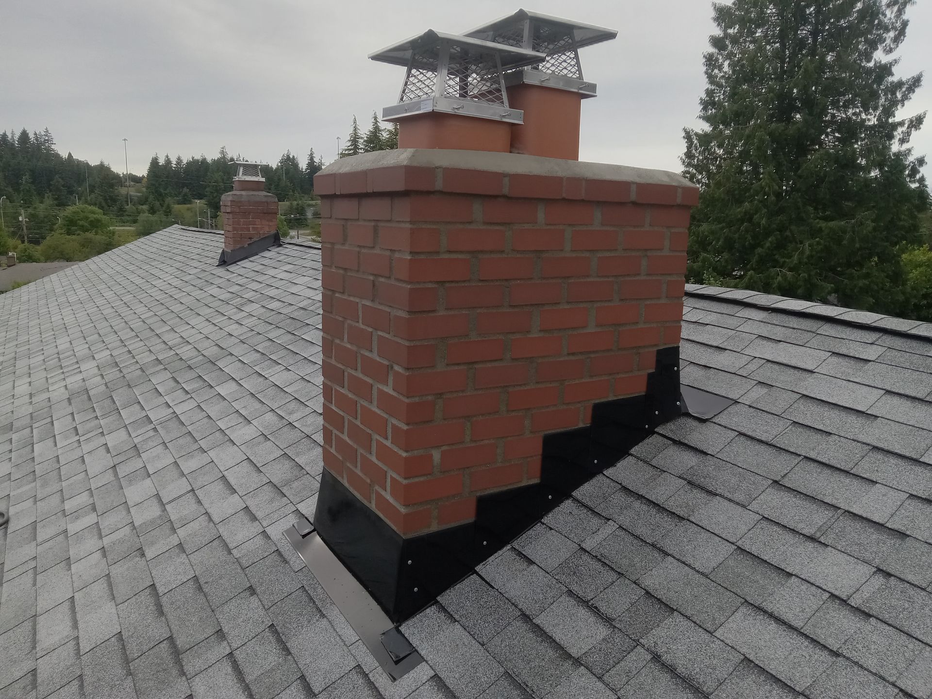 A brick chimney on top of a roof with trees in the background.