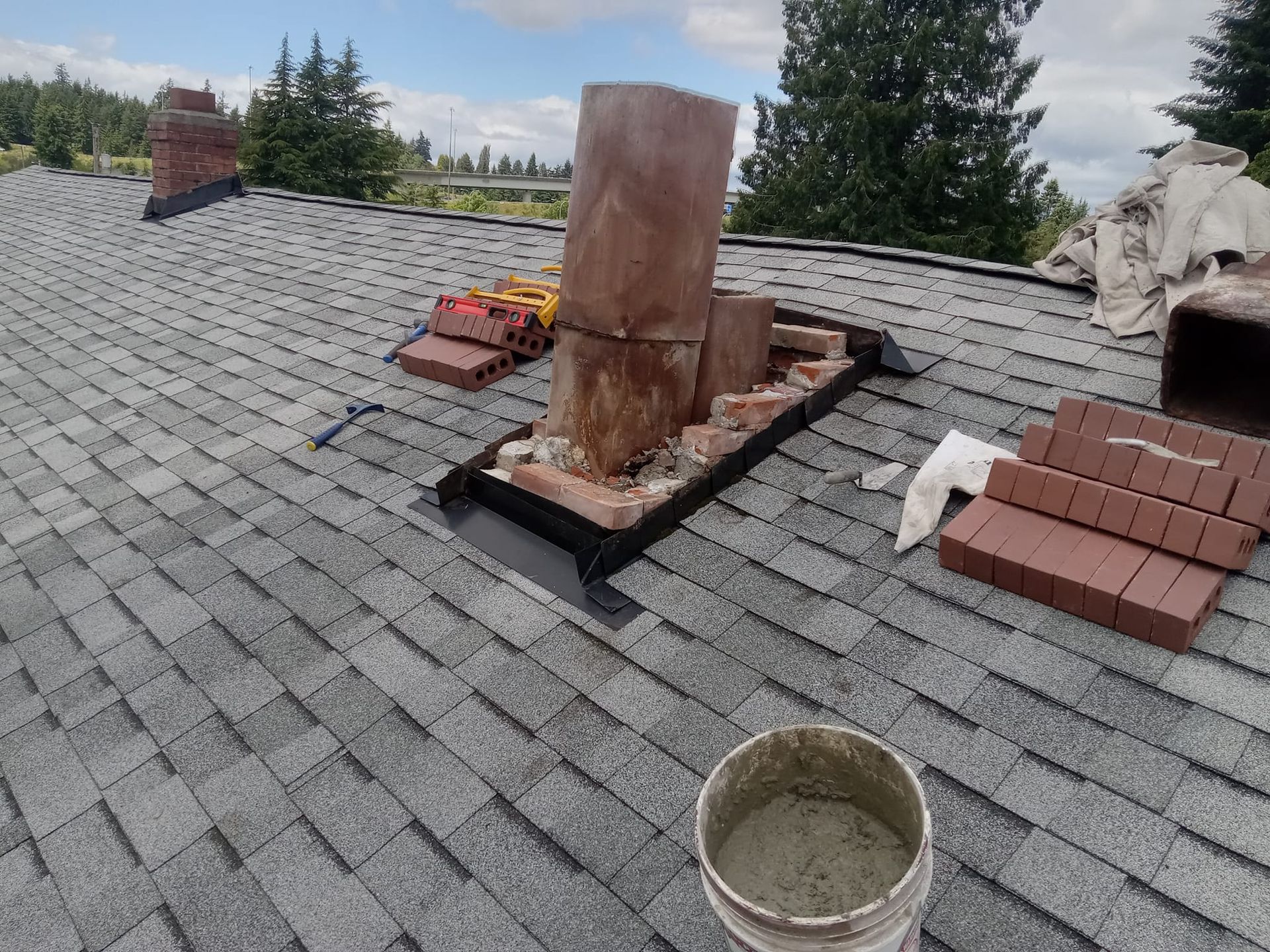 A bucket of cement is sitting on top of a roof next to a chimney.